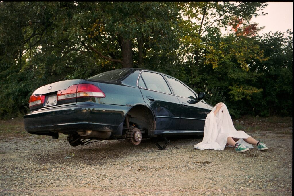 Person in sheet sits by car with no wheels.